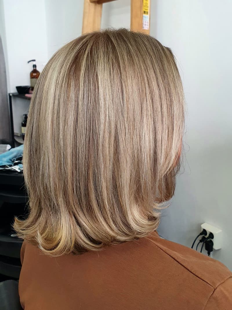 Axellång blond bob med kalla folieslingor och raka, mjukt inåtböjda toppar, fotograferad bakifrån i salongen